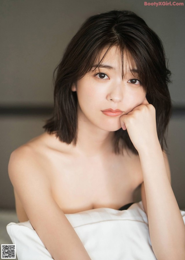 A woman sitting on top of a bed with her hand on her chin.