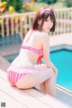 A woman in a pink and white striped bikini sitting by a pool.