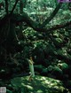 A woman in a white dress standing on a rock in the woods.