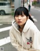 A woman in a white hoodie sitting on the street.